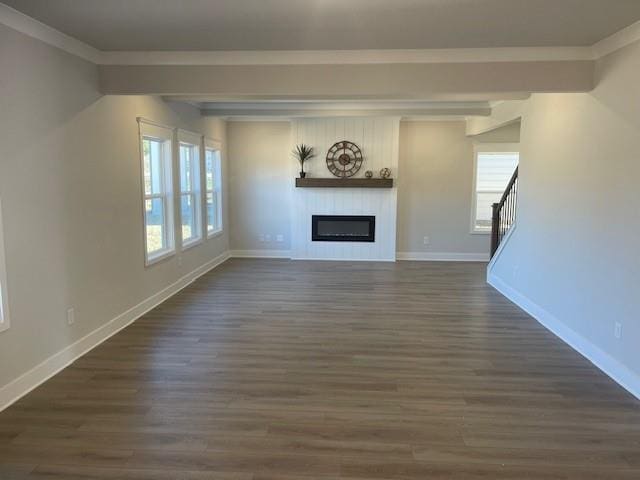 unfurnished living room featuring a glass covered fireplace, a healthy amount of sunlight, dark wood finished floors, and baseboards