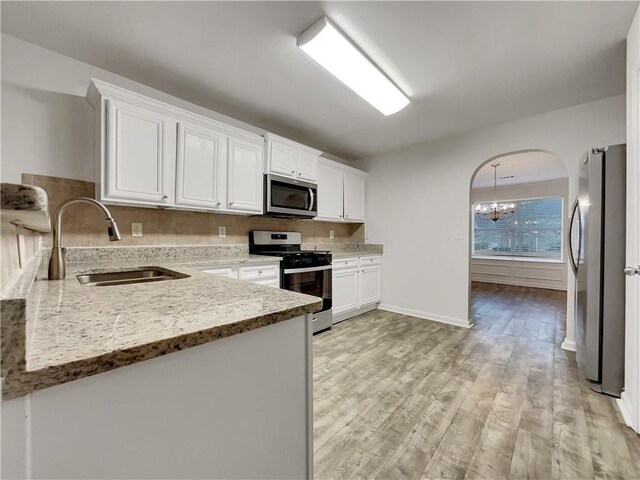 kitchen with sink, appliances with stainless steel finishes, a notable chandelier, light stone counters, and white cabinetry