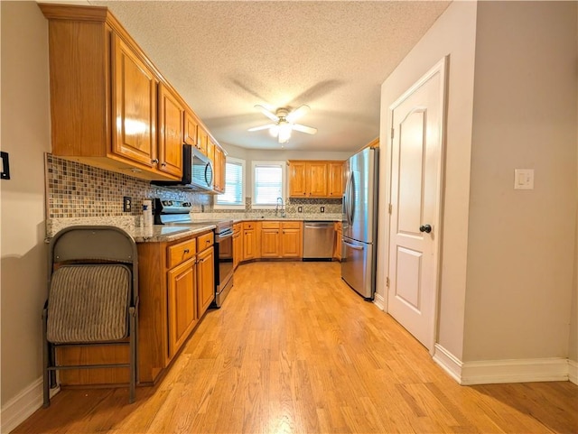 kitchen with stainless steel appliances, ceiling fan, backsplash, light wood-type flooring, and light stone counters