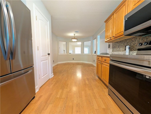 kitchen with a textured ceiling, stainless steel appliances, backsplash, hanging light fixtures, and light hardwood / wood-style flooring