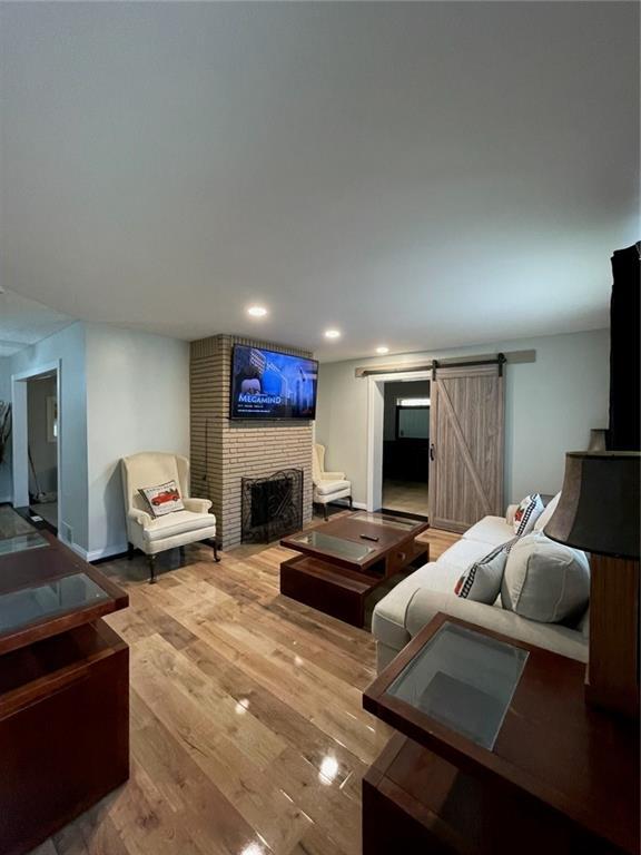 living room featuring a brick fireplace, wood-type flooring, and a barn door