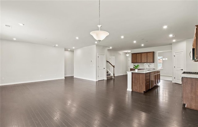 kitchen with decorative light fixtures, dark wood-type flooring, tasteful backsplash, an island with sink, and sink