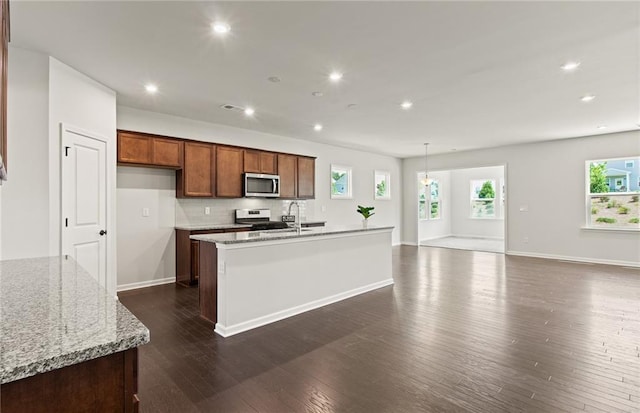 kitchen featuring a kitchen island with sink, backsplash, light stone counters, and stainless steel appliances