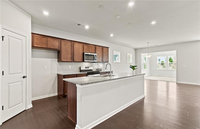 kitchen featuring pendant lighting, stainless steel appliances, decorative backsplash, sink, and a kitchen island with sink