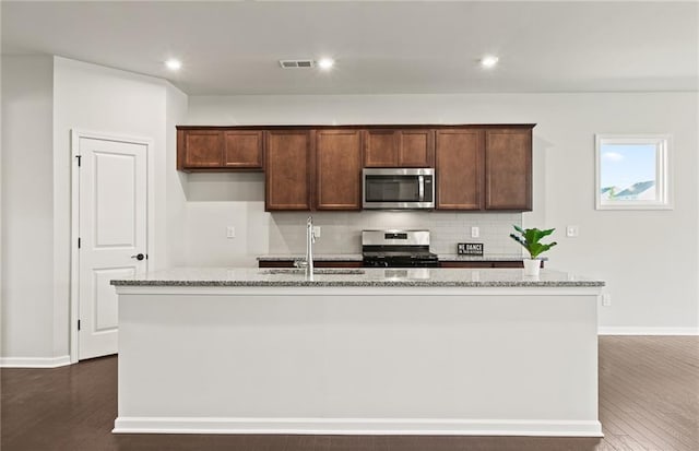 kitchen with light stone counters, sink, appliances with stainless steel finishes, and a center island with sink