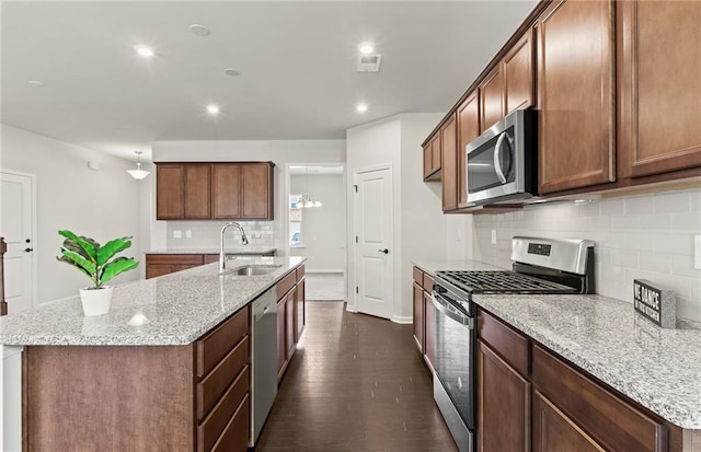 kitchen with light stone countertops, stainless steel appliances, sink, dark hardwood / wood-style floors, and a center island with sink