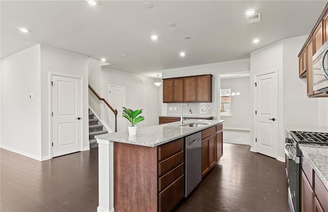 kitchen featuring dark hardwood / wood-style floors, sink, an island with sink, stainless steel appliances, and light stone counters