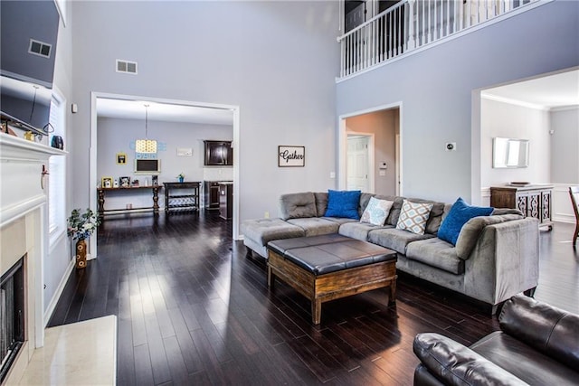 living room featuring crown molding, a fireplace, dark hardwood / wood-style floors, and a high ceiling