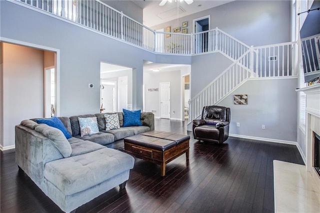 living room with ceiling fan, dark hardwood / wood-style floors, a fireplace, and a towering ceiling