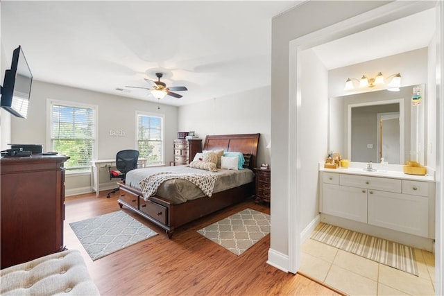 bedroom featuring connected bathroom, light hardwood / wood-style flooring, ceiling fan, and sink