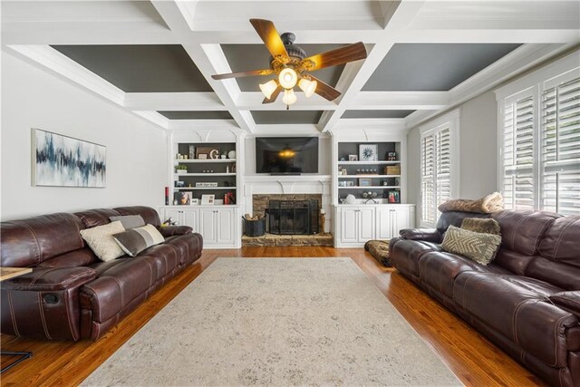 living room featuring built in shelves, ceiling fan, a stone fireplace, and wood-type flooring