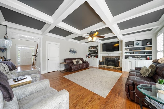 living room with built in features, ceiling fan, coffered ceiling, and a stone fireplace