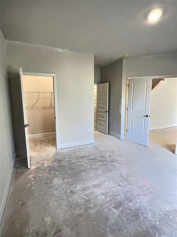 unfurnished bedroom with a spacious closet, a closet, and concrete flooring