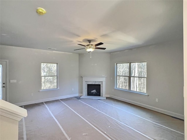 unfurnished living room with a premium fireplace, plenty of natural light, and ceiling fan