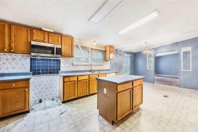 kitchen featuring a center island, brown cabinets, light countertops, stainless steel microwave, and a sink