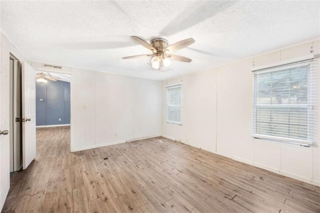 empty room featuring light wood-type flooring, visible vents, ceiling fan, and a textured ceiling