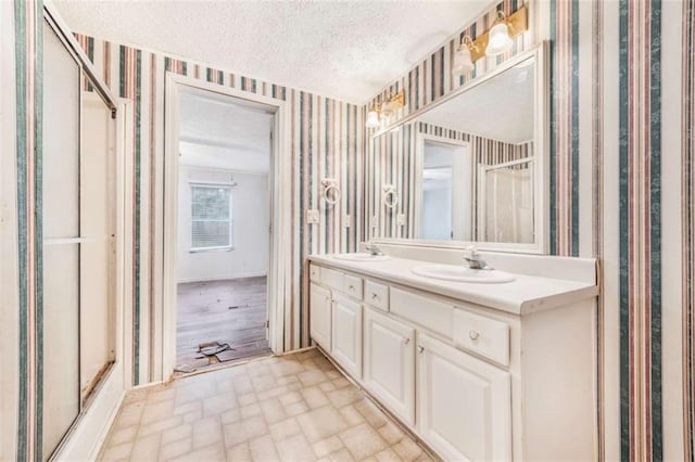 full bath featuring a stall shower, a sink, a textured ceiling, and wallpapered walls