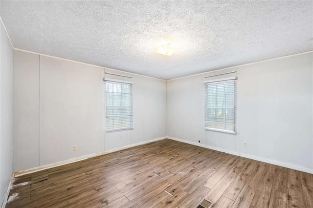 spare room featuring visible vents, plenty of natural light, a textured ceiling, and wood finished floors