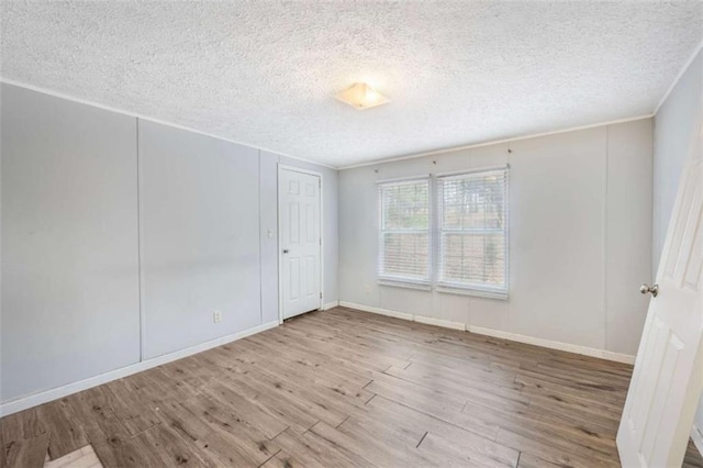 spare room featuring baseboards, light wood-style flooring, ornamental molding, and a textured ceiling