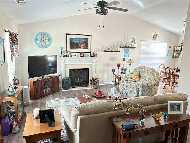 living room with light hardwood / wood-style floors, a high end fireplace, lofted ceiling, and ceiling fan