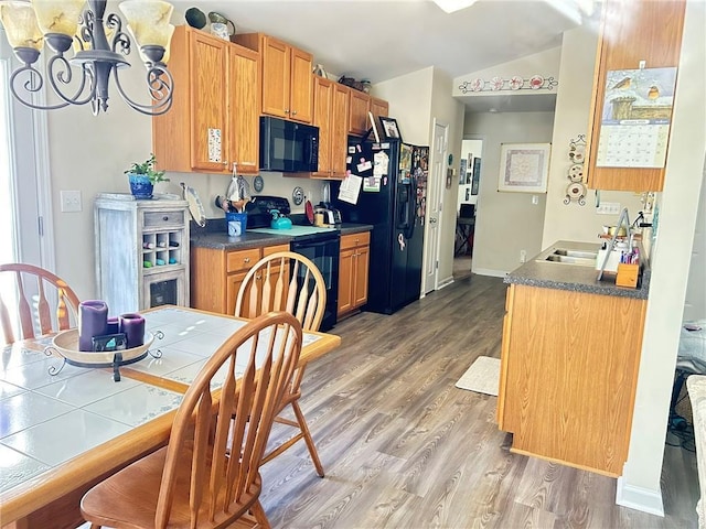 kitchen with black appliances, wood-type flooring, an inviting chandelier, sink, and vaulted ceiling