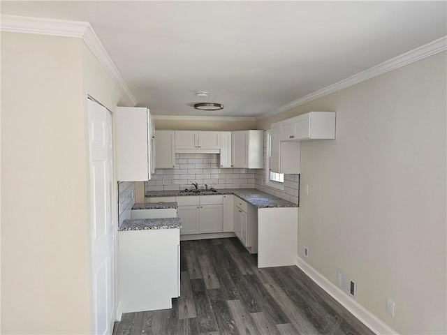 kitchen featuring dark wood-type flooring, crown molding, dark stone counters, decorative backsplash, and white cabinets