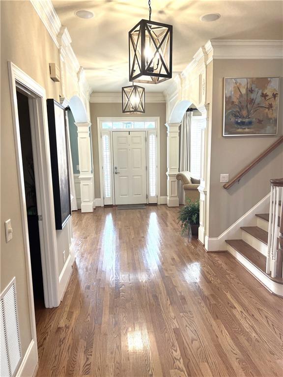 foyer featuring stairway, crown molding, ornate columns, visible vents, and arched walkways