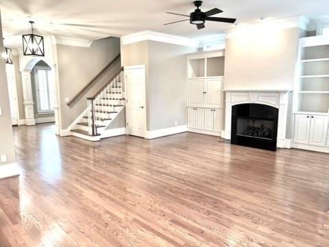 unfurnished living room with stairway, a ceiling fan, wood finished floors, arched walkways, and a fireplace