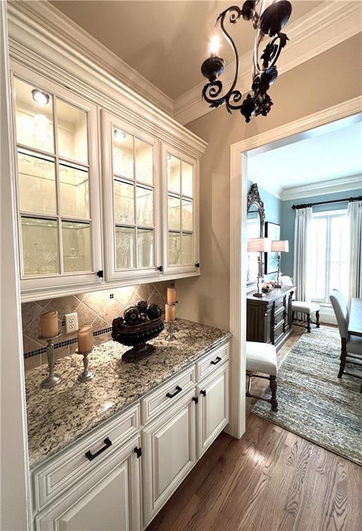 bar with an inviting chandelier, decorative backsplash, dark wood finished floors, and ornamental molding