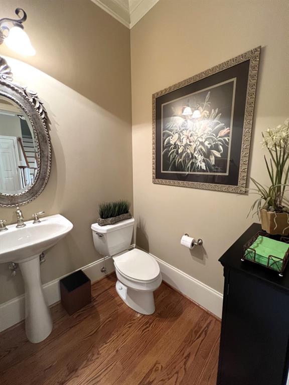 half bathroom with toilet, wood finished floors, baseboards, and a sink