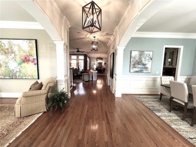 hallway with dark wood finished floors, decorative columns, crown molding, and a decorative wall