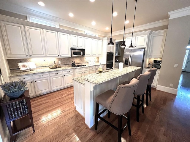 kitchen featuring a breakfast bar area, decorative light fixtures, white cabinetry, an island with sink, and stainless steel appliances