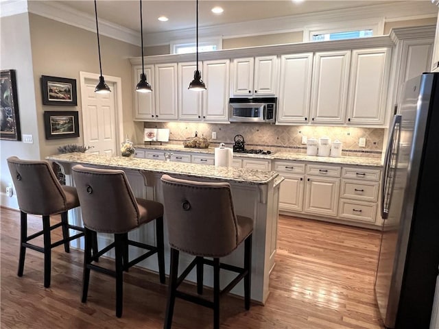 kitchen featuring stainless steel appliances, hanging light fixtures, a kitchen breakfast bar, and light stone counters