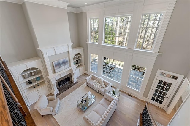 living area featuring a fireplace with flush hearth, crown molding, a high ceiling, and wood finished floors