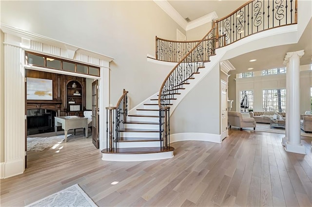 foyer with ornamental molding, a fireplace, ornate columns, and wood finished floors