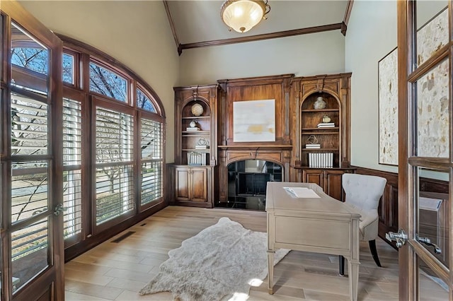 office space featuring visible vents, crown molding, light wood-type flooring, a glass covered fireplace, and high vaulted ceiling