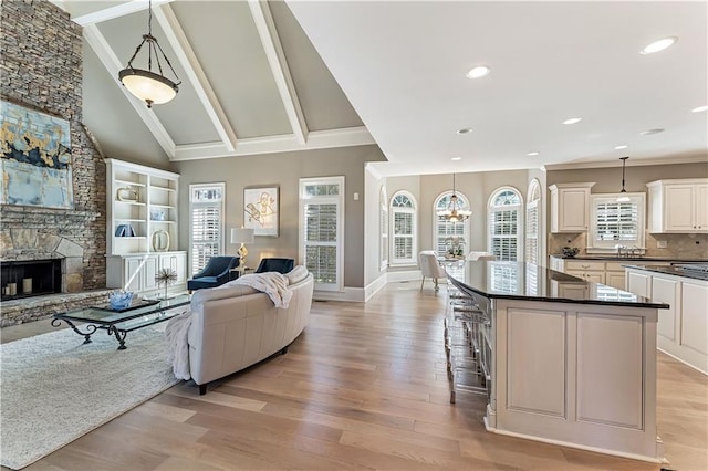 interior space with beam ceiling, high vaulted ceiling, ornamental molding, a fireplace, and light wood finished floors