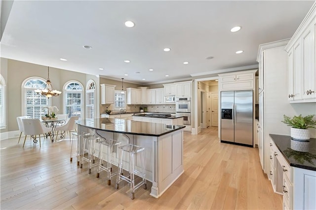 kitchen with a large island, light wood-style flooring, a kitchen breakfast bar, stainless steel appliances, and decorative backsplash