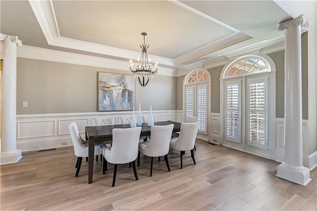 dining space with a raised ceiling, an inviting chandelier, light wood-style flooring, and ornate columns