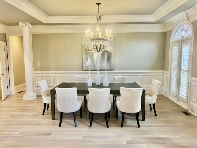 dining area featuring ornate columns, crown molding, light wood-style floors, and an inviting chandelier