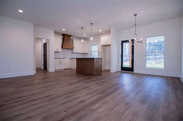 kitchen with wall chimney range hood, white cabinetry, hanging light fixtures, a notable chandelier, and a kitchen island