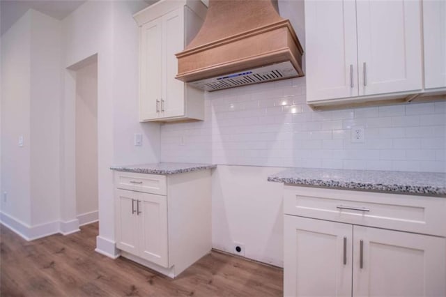 kitchen with light hardwood / wood-style flooring, premium range hood, white cabinetry, light stone counters, and decorative backsplash