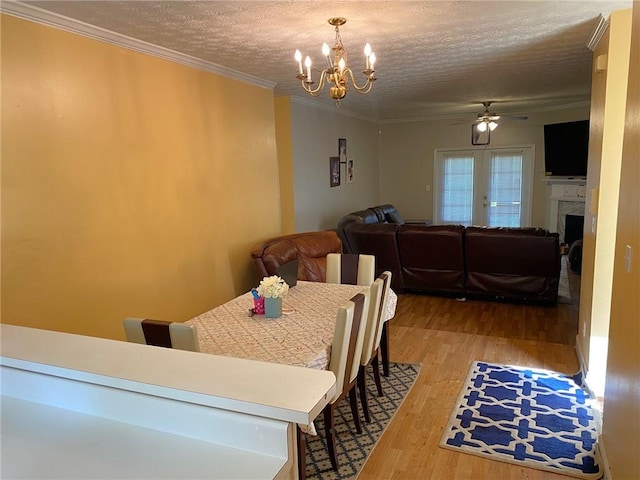 dining space with ceiling fan with notable chandelier, a textured ceiling, french doors, light hardwood / wood-style floors, and crown molding