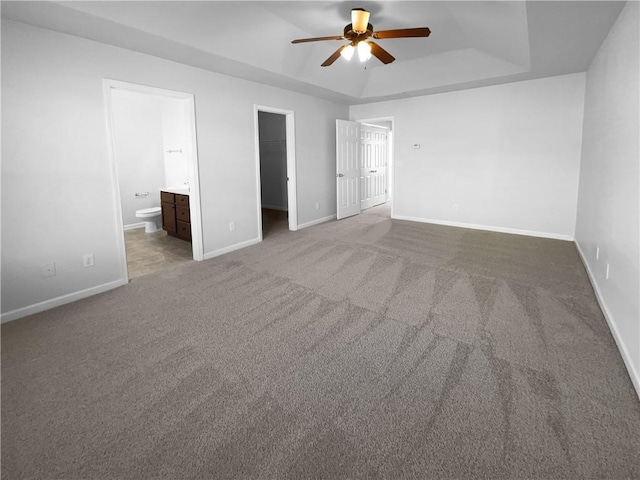 unfurnished bedroom featuring a walk in closet, a raised ceiling, connected bathroom, and baseboards