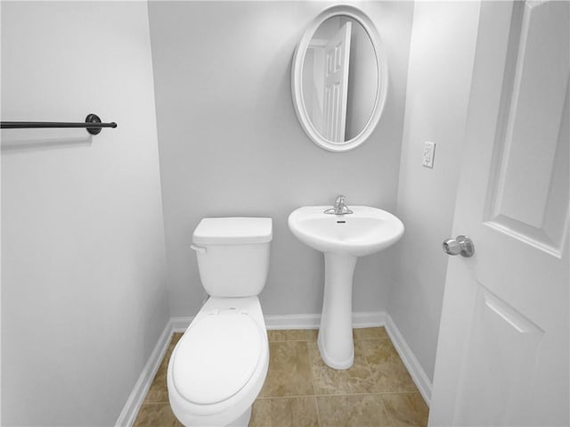 half bath with toilet, baseboards, and tile patterned floors