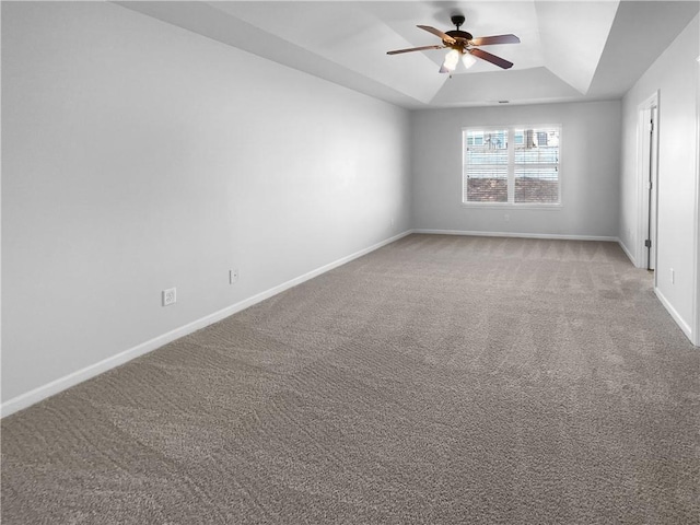 carpeted spare room featuring a ceiling fan, a tray ceiling, and baseboards