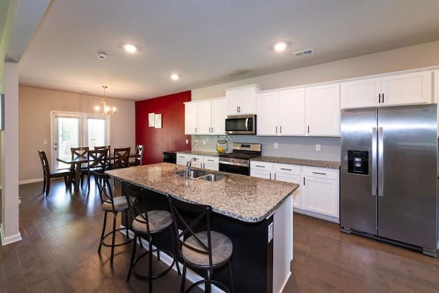 kitchen featuring stainless steel appliances, a sink, a chandelier, light stone countertops, and white cabinetry
