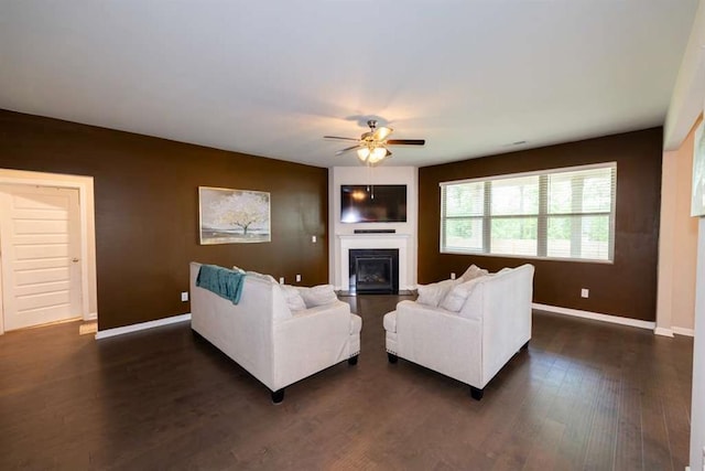 living area featuring a ceiling fan, a glass covered fireplace, baseboards, and dark wood-type flooring
