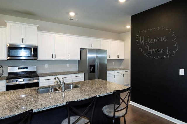 kitchen featuring stainless steel appliances, a sink, white cabinetry, light stone countertops, and a kitchen breakfast bar
