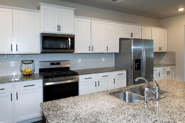 kitchen with appliances with stainless steel finishes, a sink, white cabinetry, decorative backsplash, and light stone counters